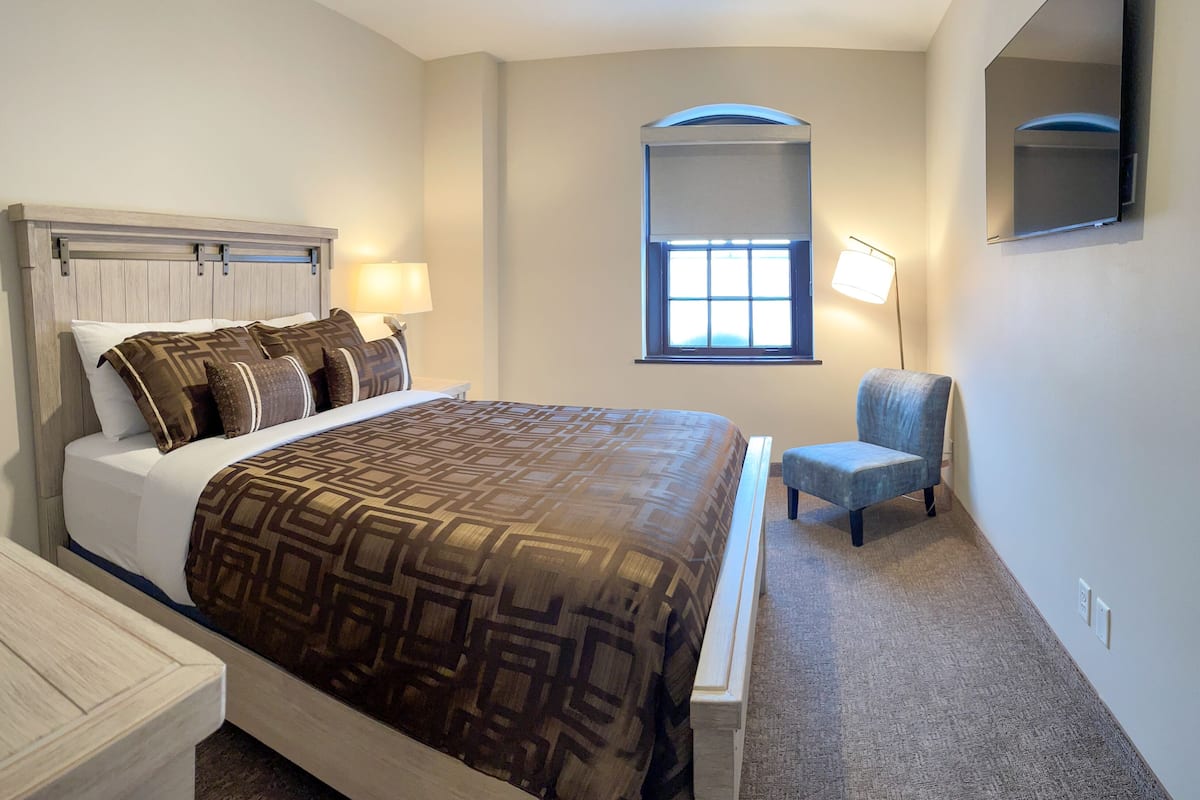 A neatly arranged bedroom with a bed, bedside table, chair, and a window with a view.