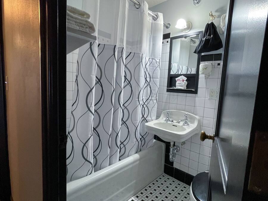 A bathroom with a white sink, a mirror, a shower curtain with a wavy pattern, and a tiled floor.