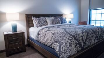 A bedroom with a wooden bed, patterned bedding, two bedside tables with lamps, and a window with blinds.