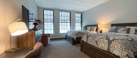 A bedroom with a large bed, a desk with a lamp, a chair, and a dresser.