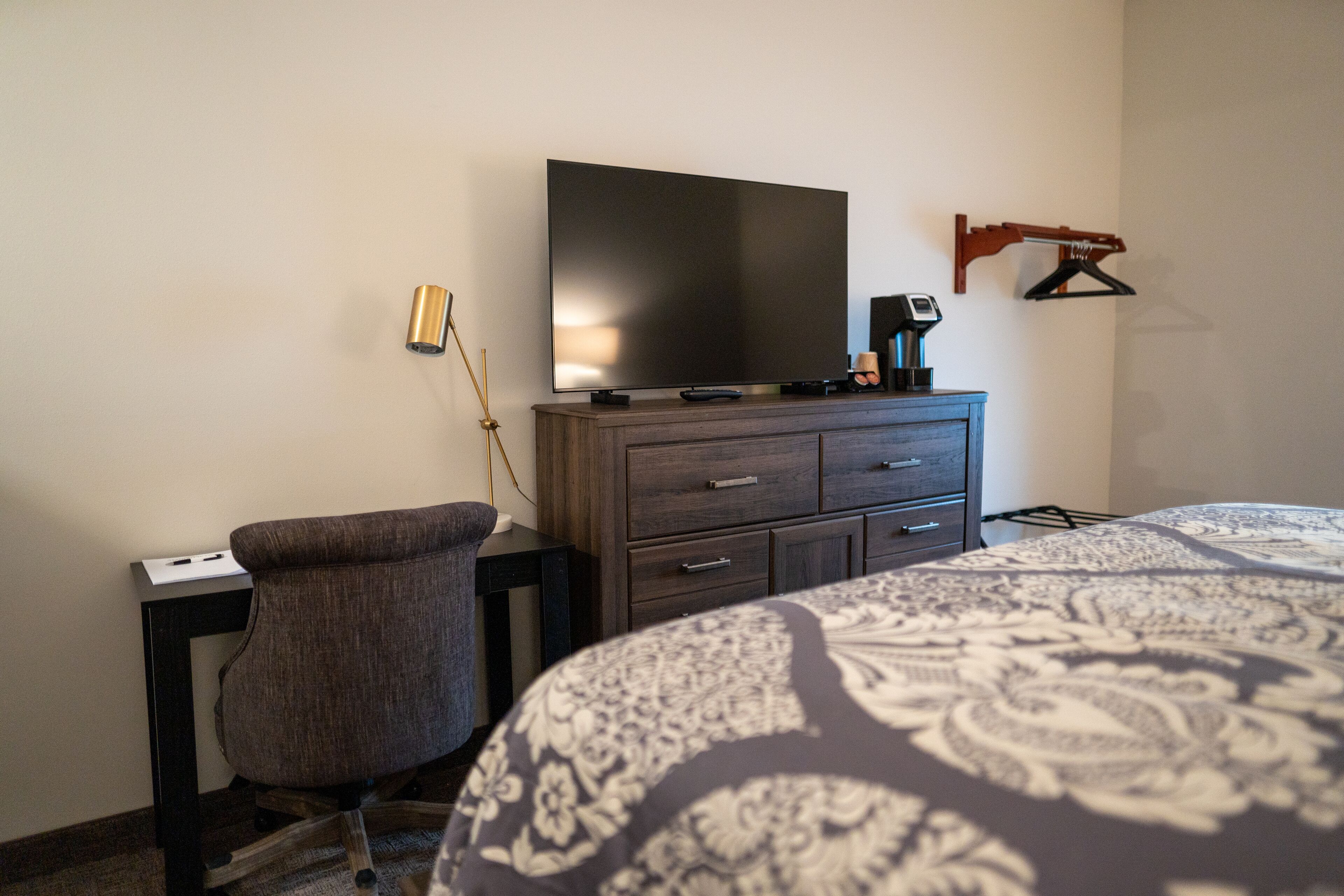 Habitación de hotel con cama, escritorio, silla, televisor y cómoda.