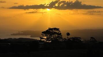 A sunset over a coastal landscape with silhouettes of trees and distant landforms.
