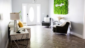 En moderne stue med en hvid sofa, en sort lænestol, et lille bord med en lampe og en grøn vægdekoration.