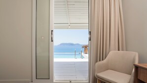 A room with a view of the sea, a chair, and a wooden floor.
