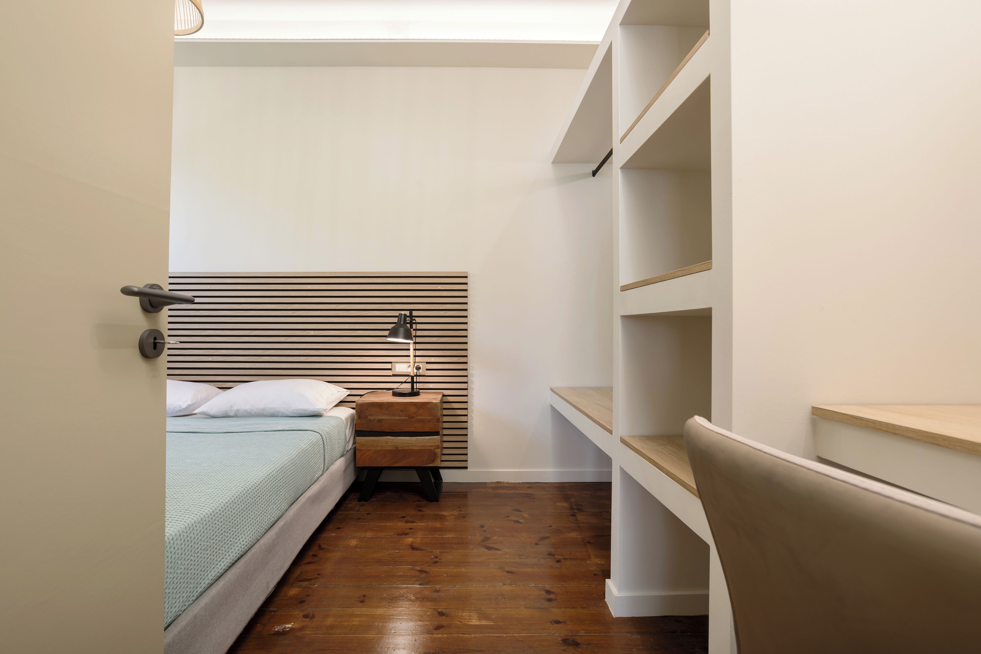 A bedroom with a bed, bedside table, lamp, and built-in shelving.