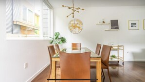 Un coin repas avec une table et des chaises en bois, un luminaire suspendu et une œuvre d’art abstraite accrochée au mur.