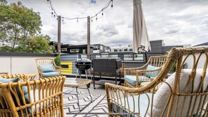 Un espace extérieur aménagé avec des meubles en osier, un barbecue et des guirlandes lumineuses.