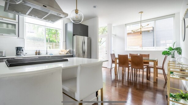 Une cuisine moderne dotée d’un îlot central, d’appareils électroménagers en acier inoxydable et d’un coin repas avec des chaises en bois et une table en verre.