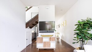 Un salon moderne avec un téléviseur à écran plat fixé à un meuble blanc, un parquet en bois et un escalier en arrière-plan.