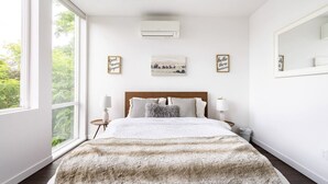 Une chambre avec une grande fenêtre, un lit recouvert d’une couverture moelleuse, des lampes de chevet et des œuvres d’art accrochées au mur.