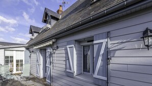 Una casa con una terraza de madera, una puerta de garaje y un ventanal con contraventanas.