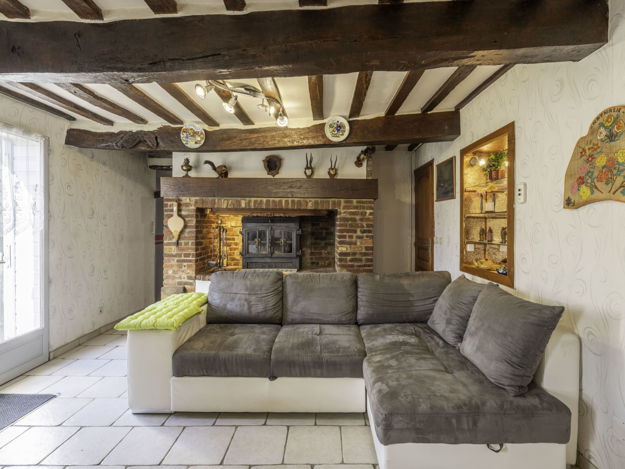 Una sala de estar acogedora con un amplio sofá seccional gris, una chimenea de ladrillo, vigas de madera a la vista y decoración artística en las paredes.