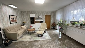 En moderne stue med sofa, lænestol, sofabord og et spiseområde med et skab.
