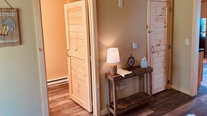 A hallway with wooden doors and a console table with a lamp and decorative items. - Cozy Cabin Boarding Winslow Hill Elk Viewing Area! (Benezette)