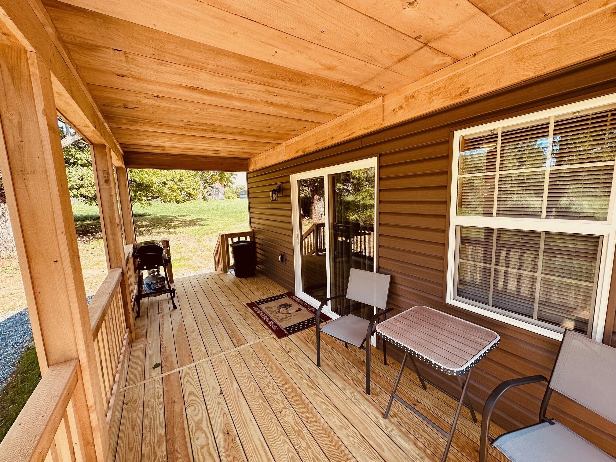 A covered porch with wooden flooring, a table and chairs, and a grill.
