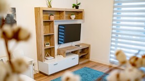 A modern living room with a wooden entertainment unit, a flat-screen TV, a white sofa, and a blue rug. - Cozy spacious studio in new building (București)