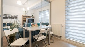A modern dining area with a glass partition, white chairs, a table with a water bottle, and a cityscape view. - Cozy spacious studio in new building (București)