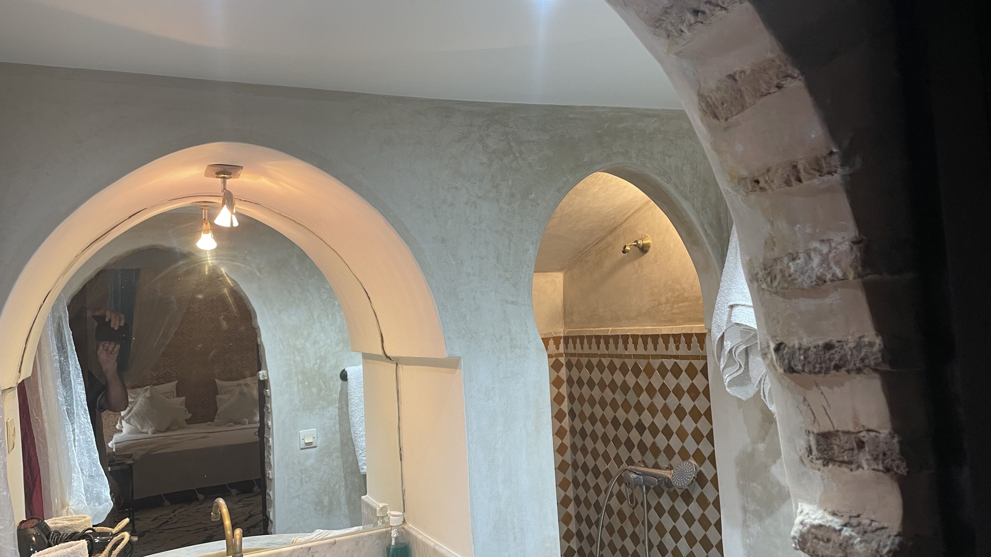 Un baño con lavamanos de mármol, un perchero y una ducha con pared de azulejos estampados.
