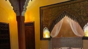Ein traditionelles marokkanisches Interieur mit einer Couch, einem Hocker und Teppichen mit Muster.