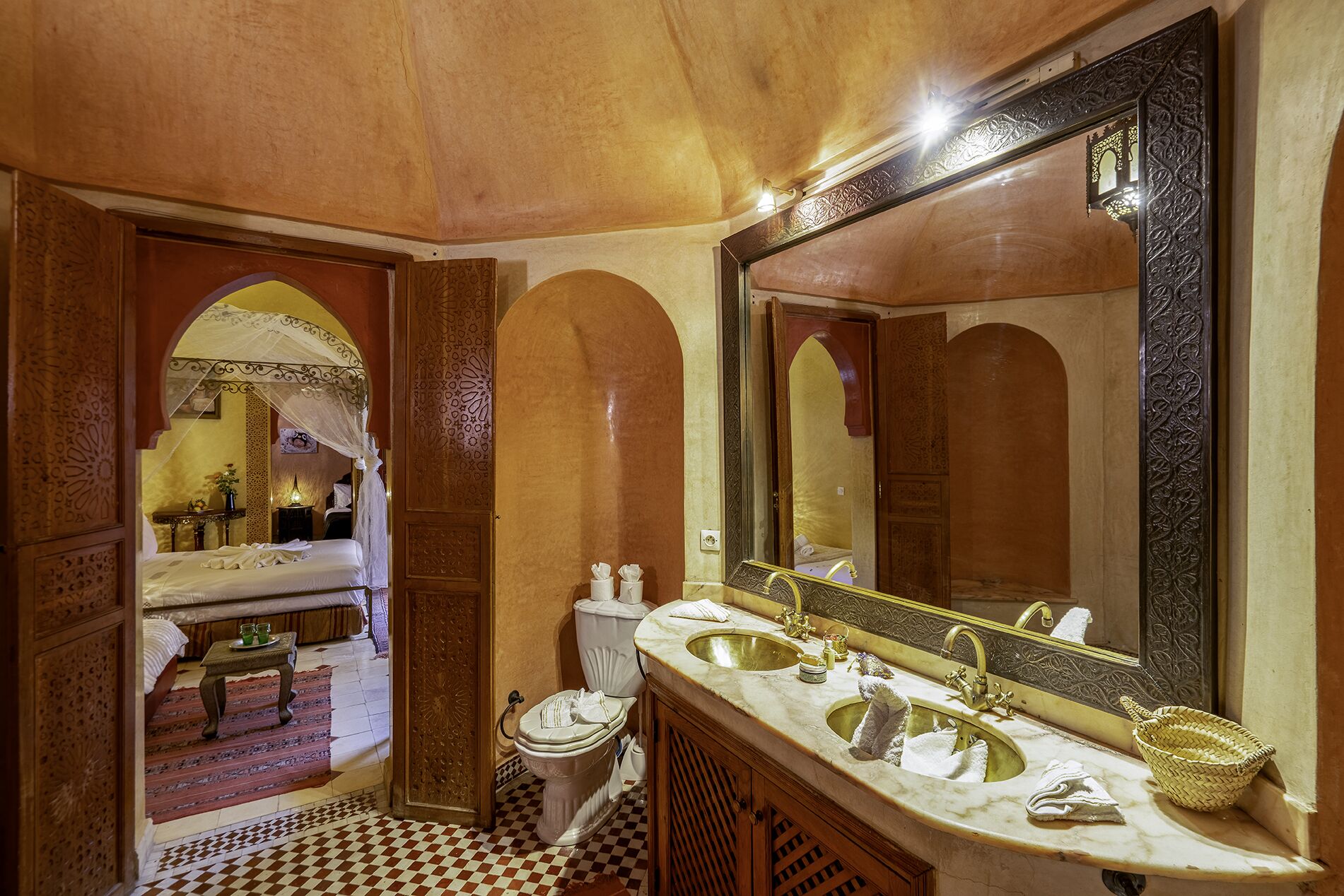 Une salle de bain traditionnelle avec un carrelage à motifs, un grand miroir, deux lavabos et des toilettes.