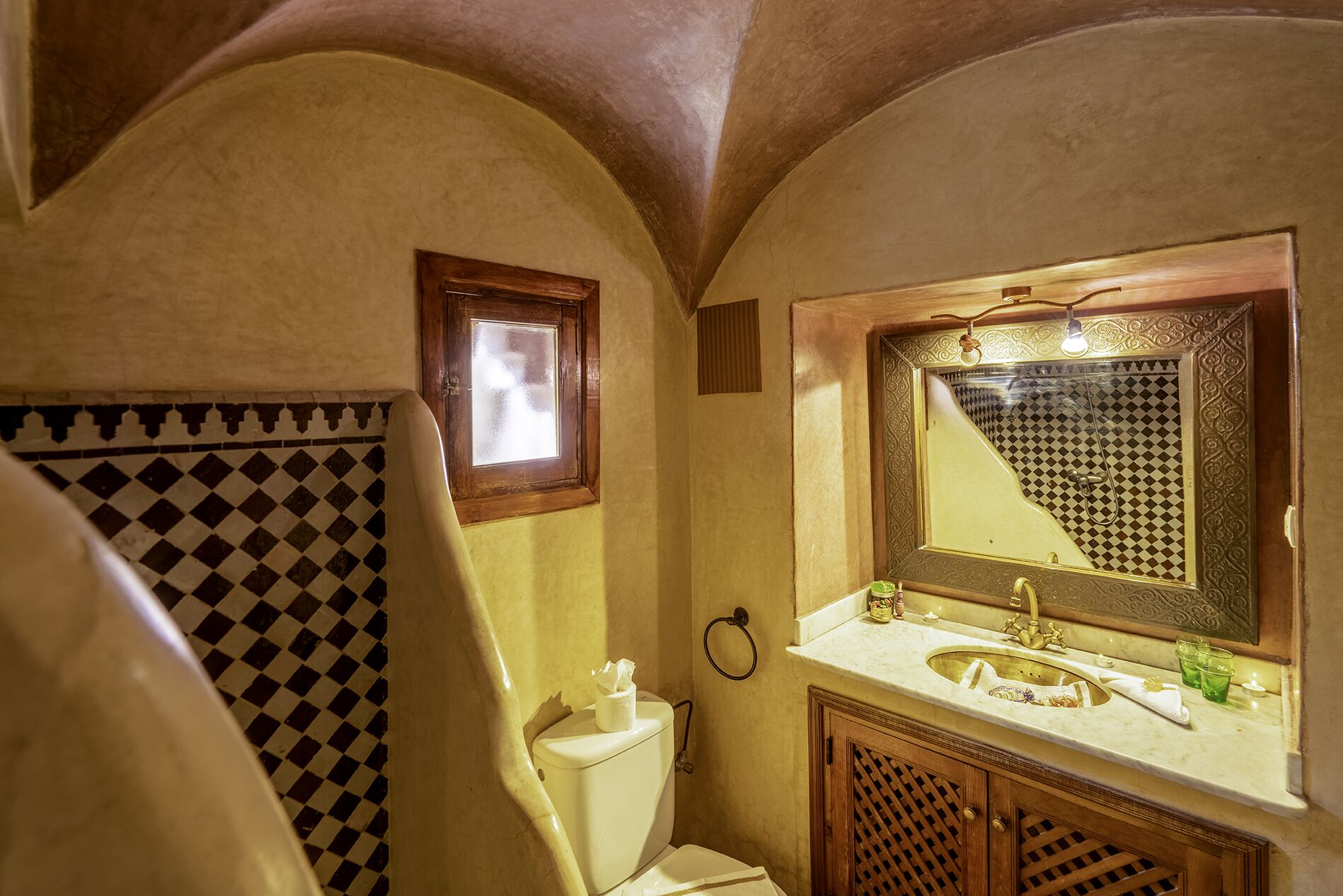 Une salle de bain avec un carrelage à motifs géométriques, des toilettes, un lavabo avec un miroir et un espace douche.