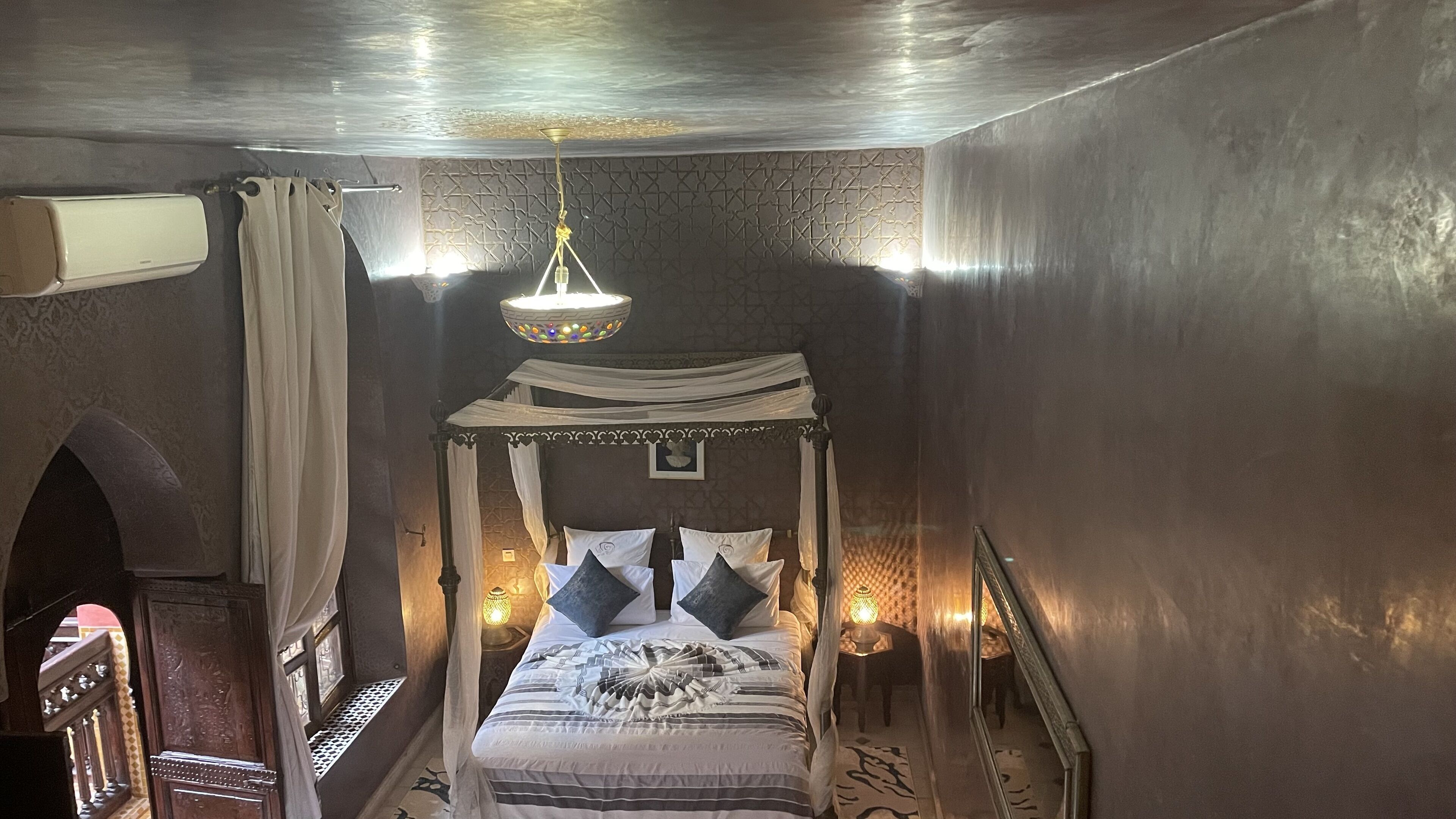 A four-poster bed with a canopy, bedside lamps, and a patterned rug.