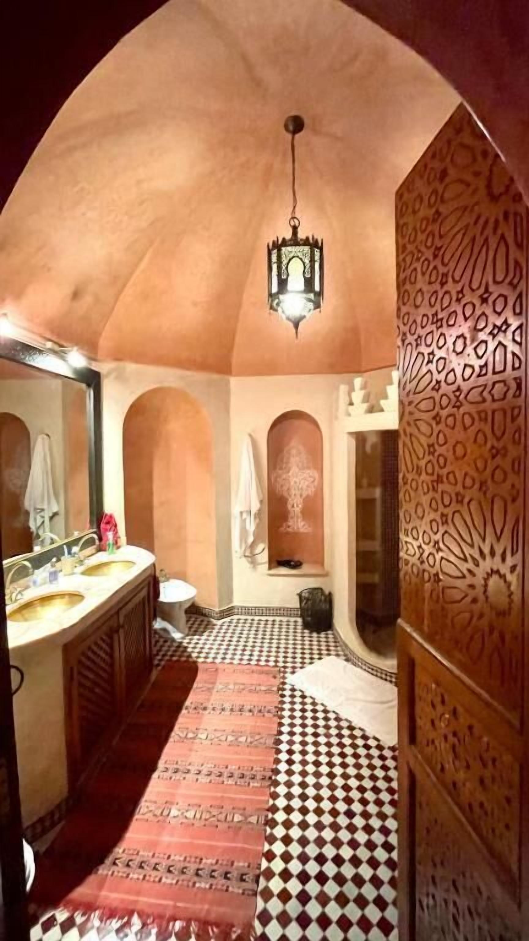 A bathroom with a checkered floor, a sink, a mirror, and a patterned wall.