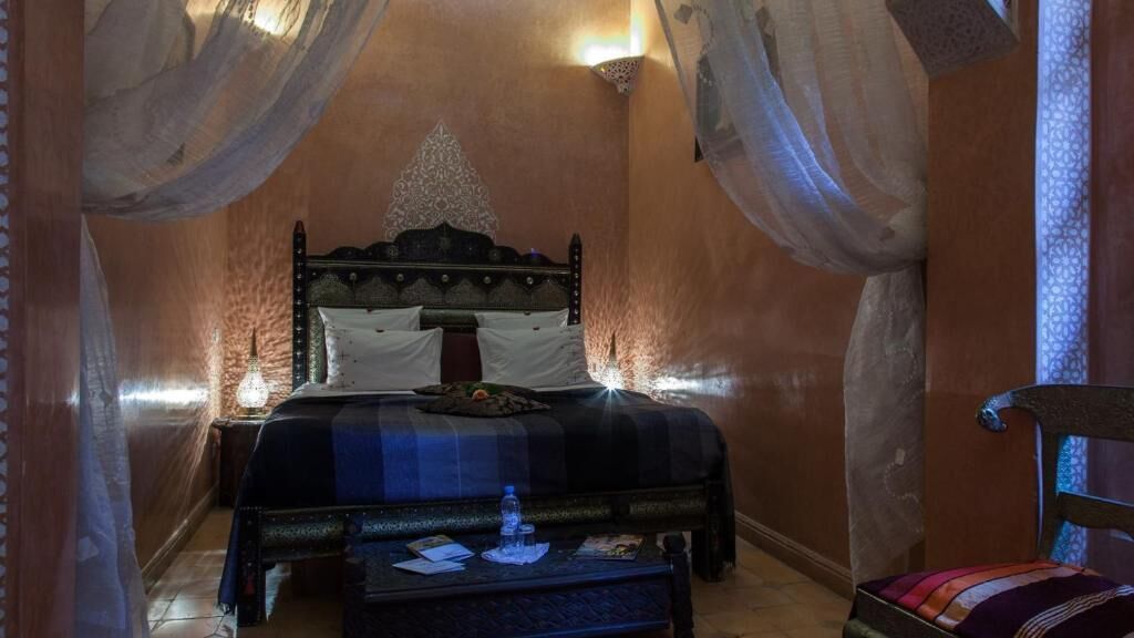 Una habitación con una cama, una mesita de noche, una mesa con una botella y una silla.
