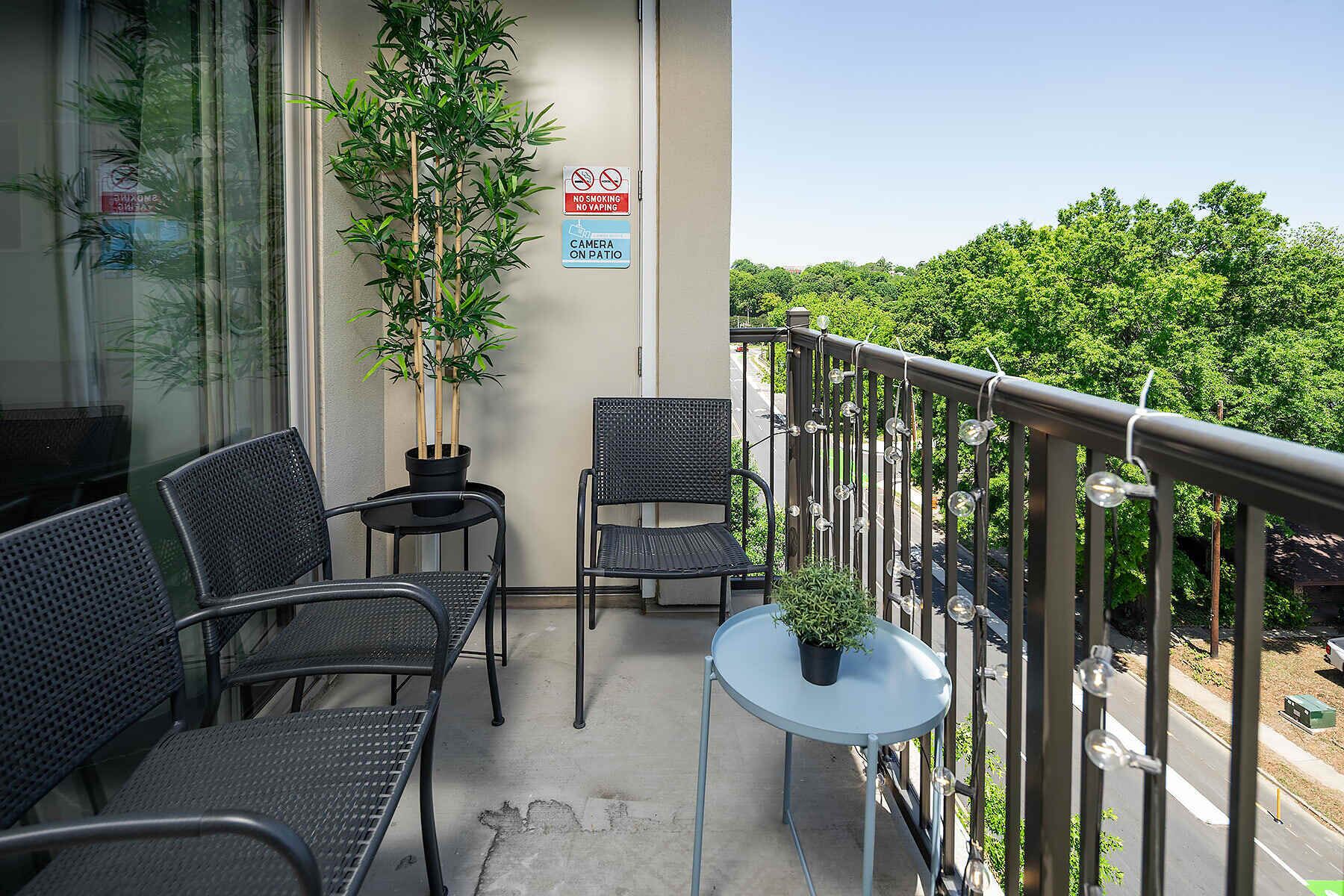 A balcony with two chairs, a small table, and a potted plant. There are signs indicating no smoking and no parking.