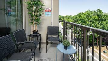A balcony with two chairs, a small table, and a potted plant. There are signs indicating no smoking and no parking.