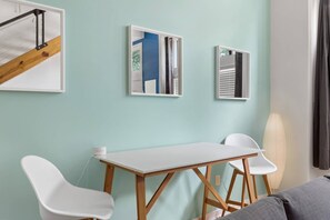 Een kamer met een witte tafel en twee witte stoelen, een houten vloer en een lichtgroene muur.