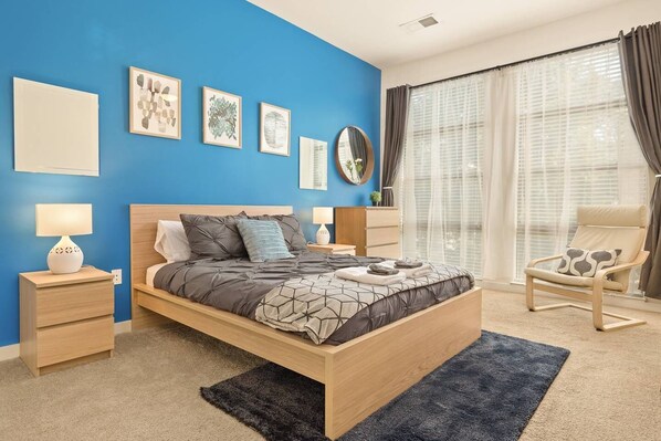 Een moderne slaapkamer met een bed, nachtkastjes, een stoel en kunst aan de muur.