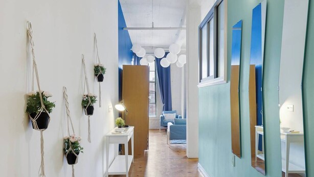 A hallway with macrame wall hangings, a white console table with a lamp, and a blue sofa in the background. - 100 Year-Old Historic Brick 2BR Loft-High Ceiling8 (Durham)