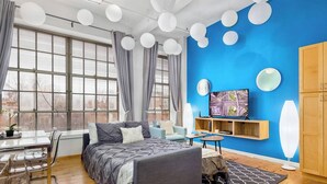A modern bedroom with a large bed, a TV, and a blue accent wall. - 100 Year-Old Historic Brick 2BR Loft-High Ceiling8 (Durham)