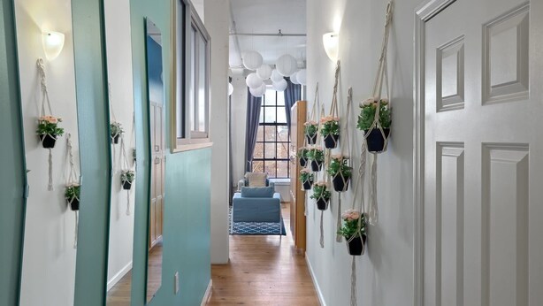 Un pasillo con puertas verde azulado, paredes blancas y colgadores de plantas de macramé.