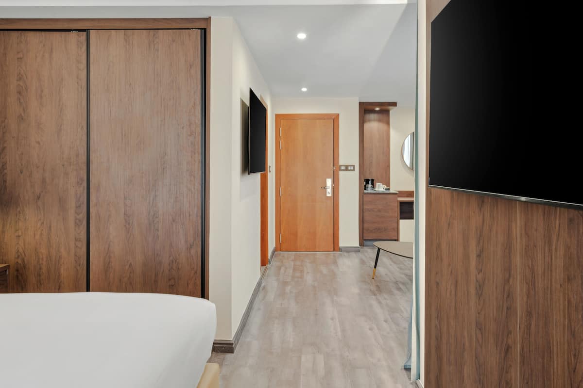 Une chambre d’hôtel avec un grand lit, une armoire en bois, une télévision et une petite salle de bain équipée d’un miroir et d’un lavabo.