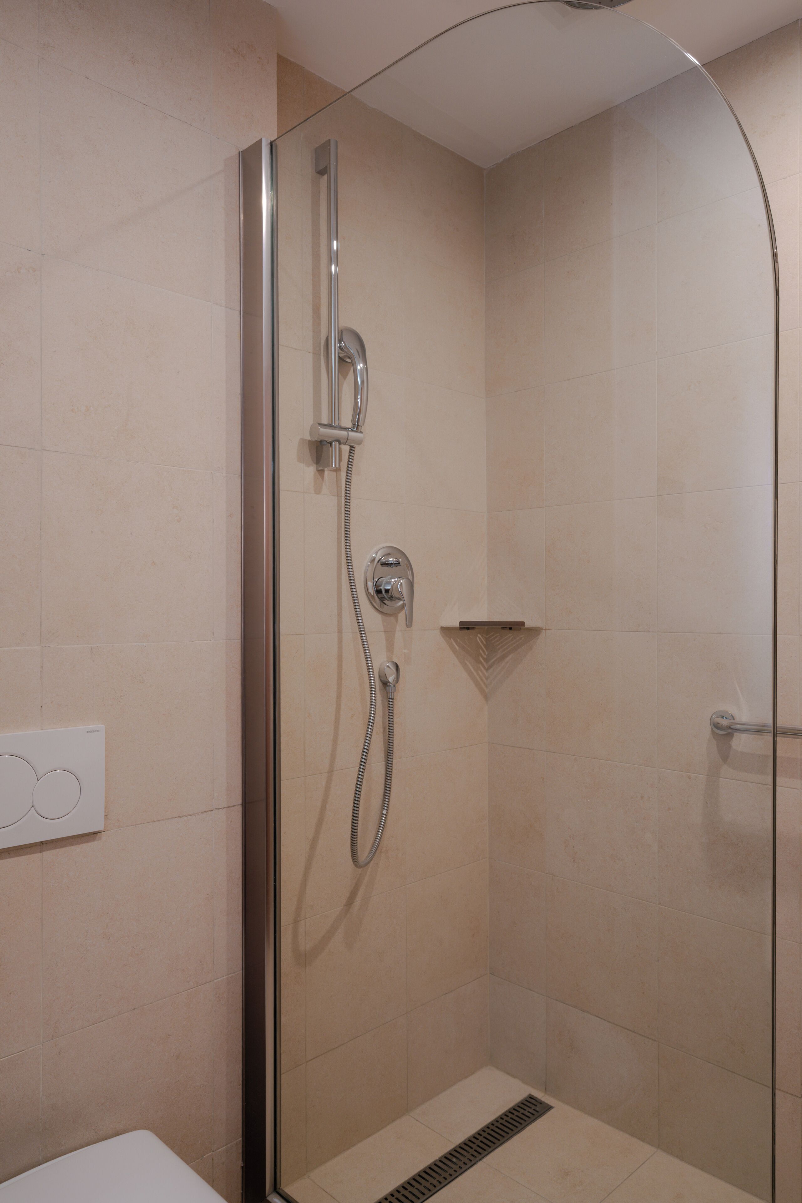 A glass-enclosed shower with a handheld showerhead and a wall-mounted faucet.