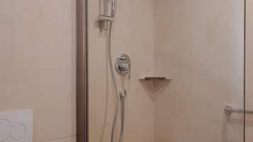 A glass-enclosed shower with a handheld showerhead and a wall-mounted faucet.