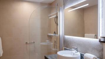 Une salle de bain moderne avec une douche à parois de verre, un lavabo rond et un grand miroir.