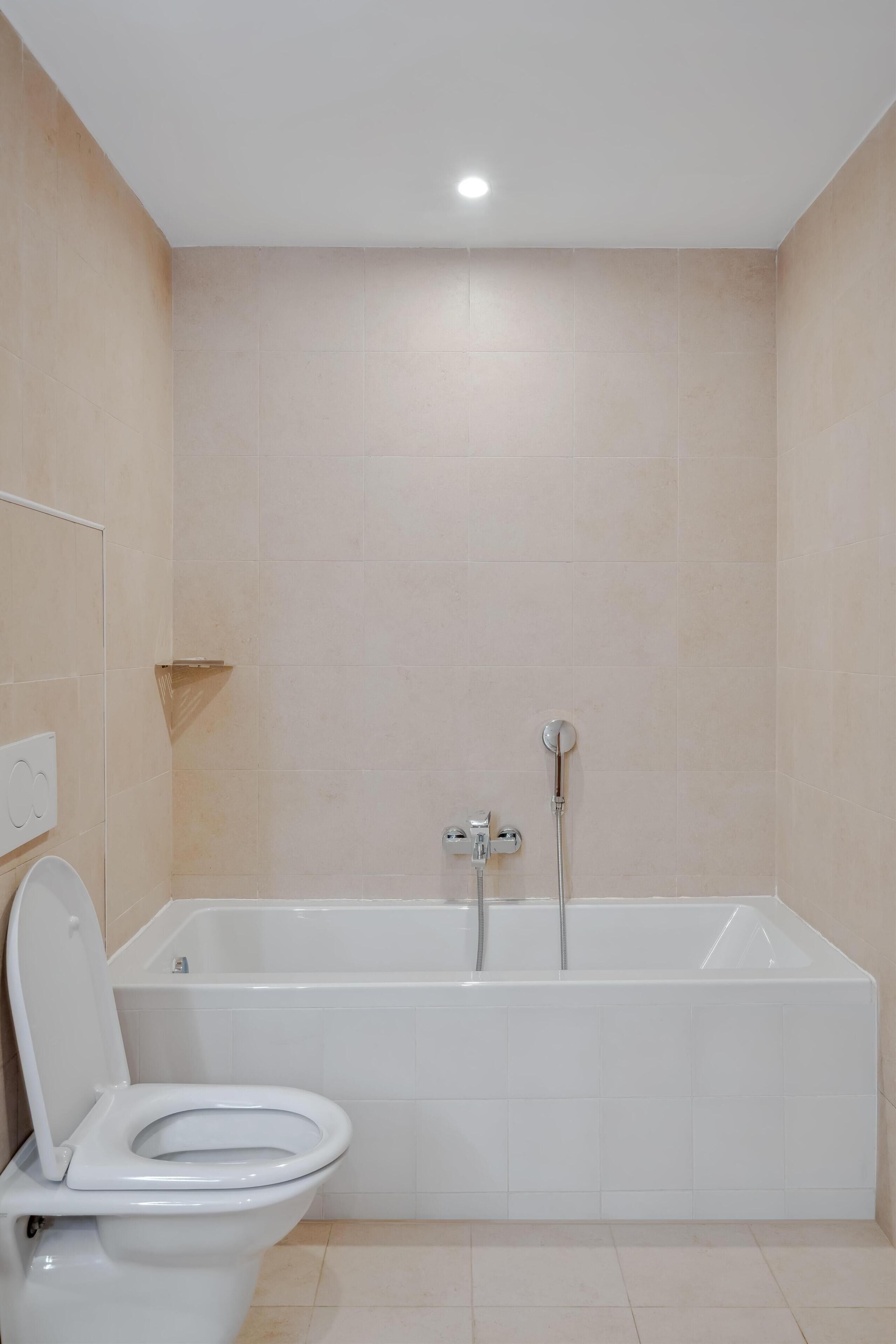 A bathroom with a white toilet, a bathtub, and beige tiled walls.