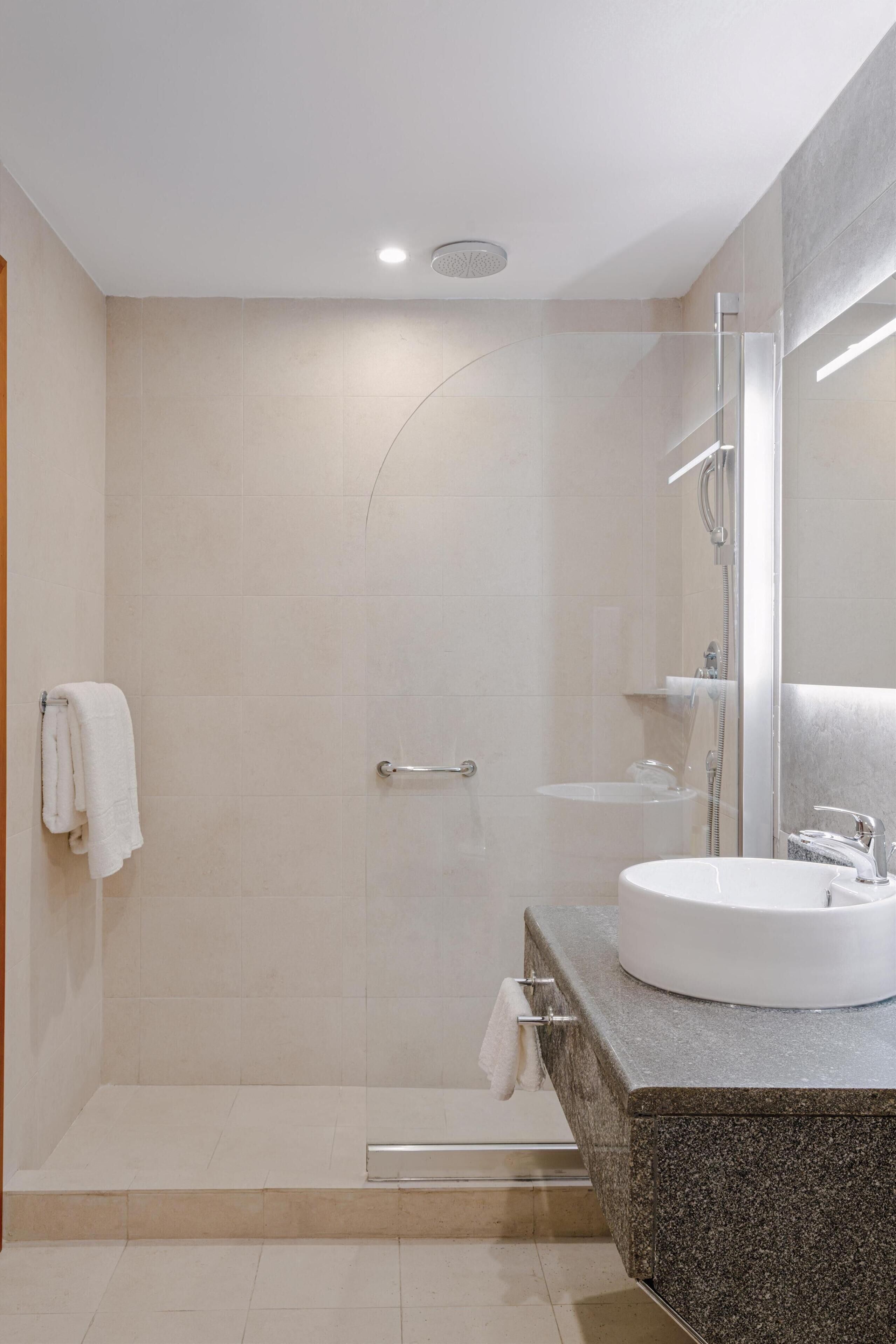 Un baño moderno con ducha de vidrio, lavamanos blanco y un espejo grande.