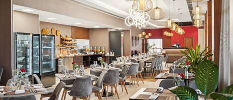 Un restaurante moderno con una larga mesa de comedor, sillas grises tapizadas y lámparas colgantes.