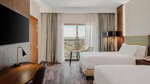 Une chambre d’hôtel avec deux lits, un bureau, une télévision et une grande fenêtre donnant sur la ville.