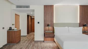 Ein Hotelzimmer mit einem großen Bett, einem Holz-Kopfteil, Nachttischen mit Lampen, einer Holzkommode und einer kleinen Küchenzeile.
