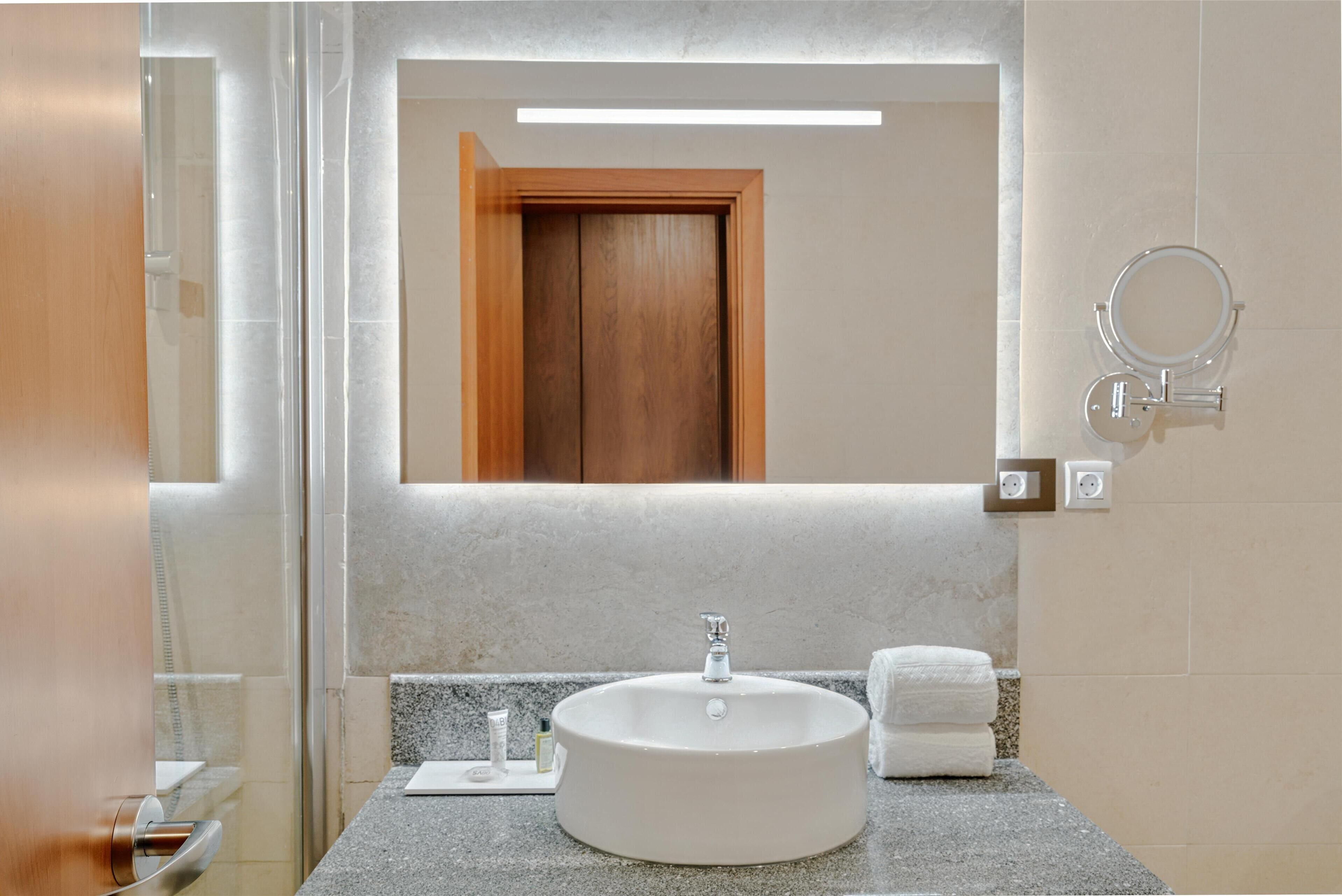 Un baño con un lavamanos redondo, un espejo y un perchero para toallas.