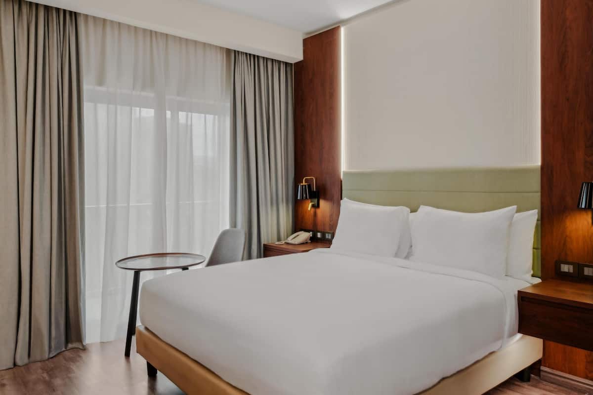 Une chambre d’hôtel avec un grand lit, une petite table, une chaise et une table de chevet avec un téléphone.