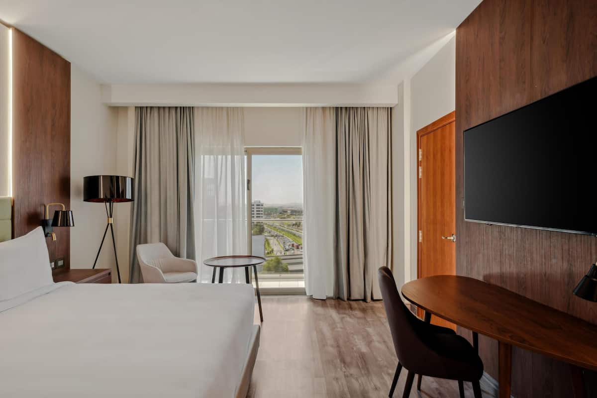 Une chambre d’hôtel avec un grand lit, un bureau, une chaise, une télévision et une vue sur la ville par la fenêtre.