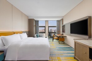 Een hotelkamer met een groot bed, een bureau, een televisie en uitzicht op de stad.