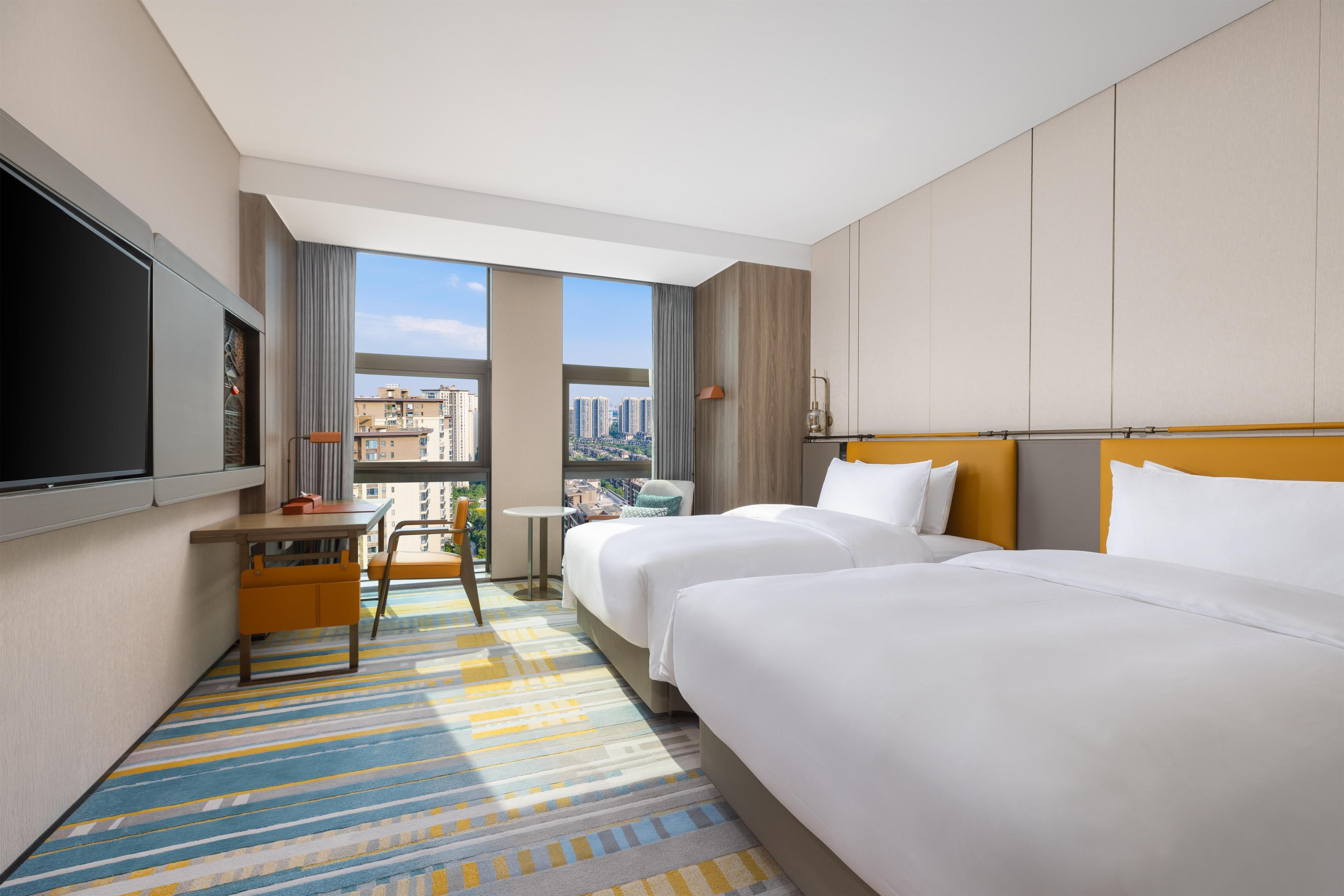 Une chambre d’hôtel avec deux lits, un bureau, une chaise, une télévision et une vue sur la ville.