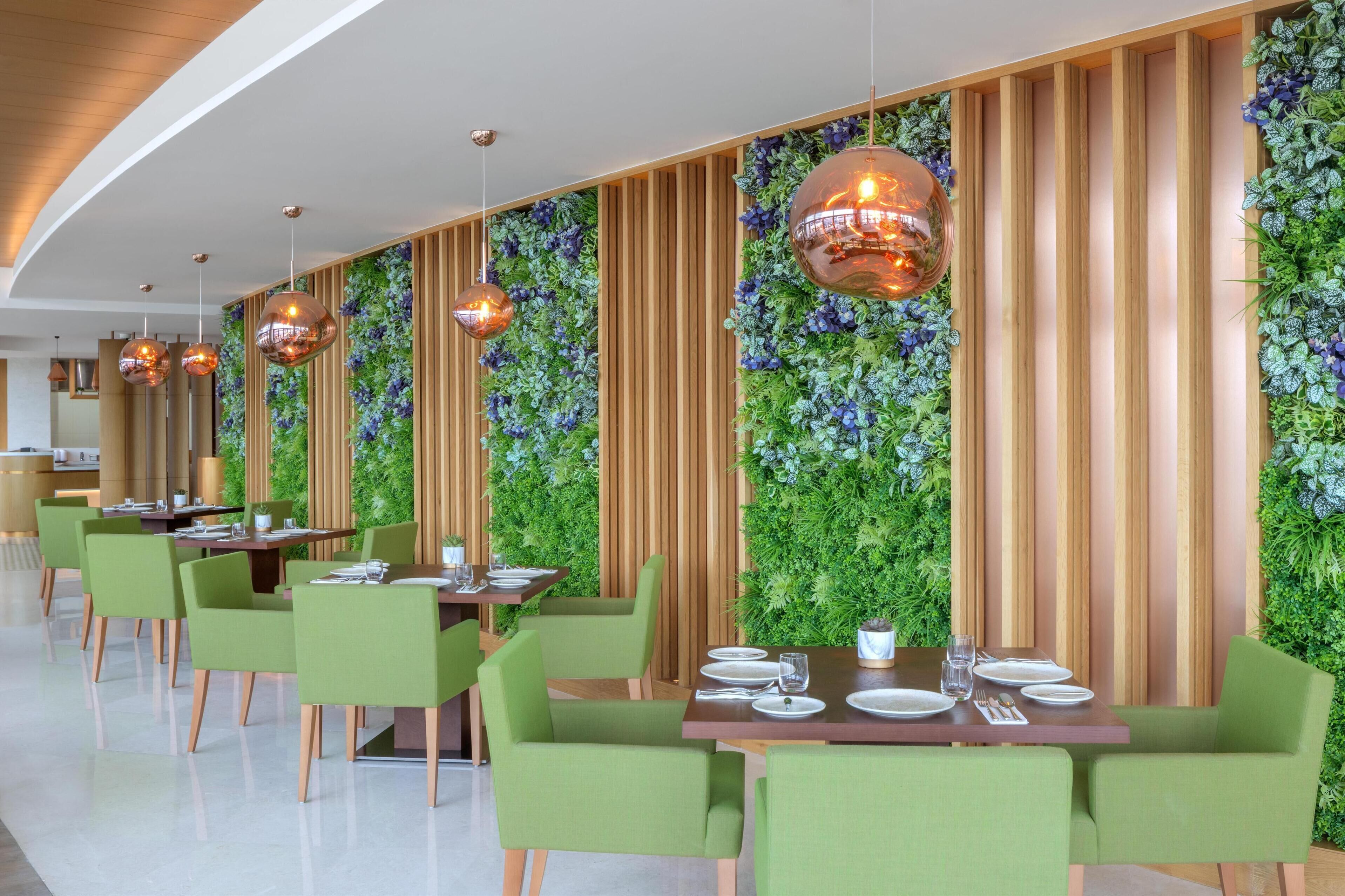 A modern restaurant with green chairs, wooden tables, and hanging copper pendant lights.